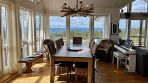 A spacious room with a wooden dining table, wicker chairs, a piano, and large windows offering a view of the outdoors. - TexasToppen, cabin in Hafjell with sauna (Øyer)