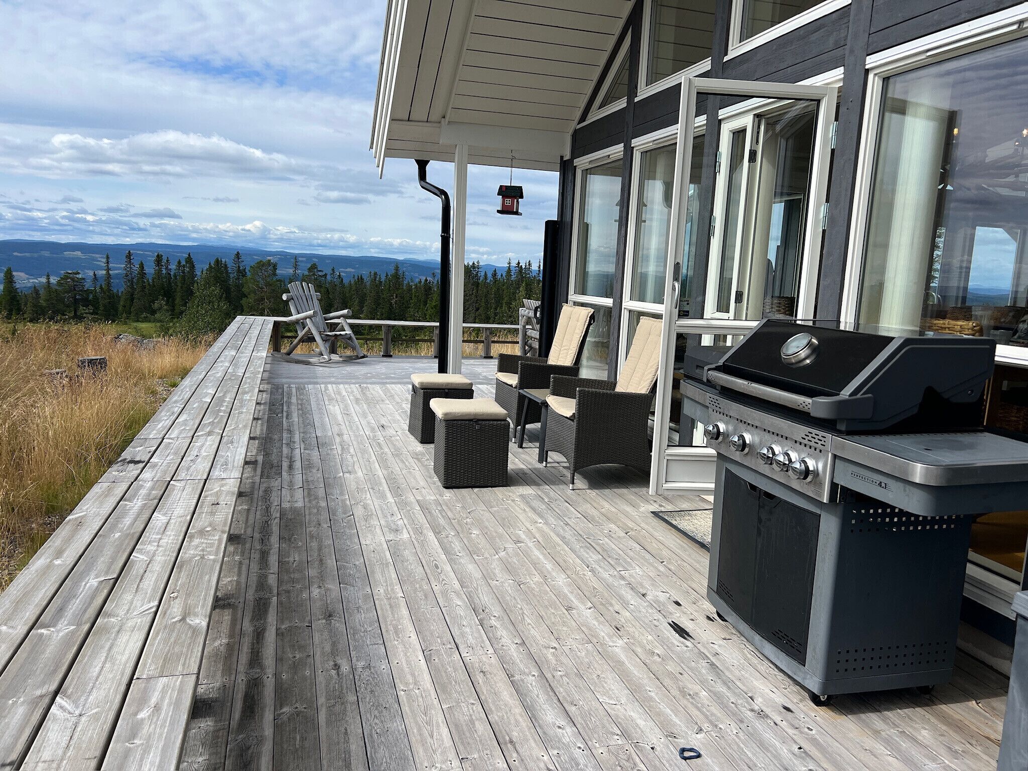 A wooden deck with outdoor furniture, a grill, and a view of the landscape.
