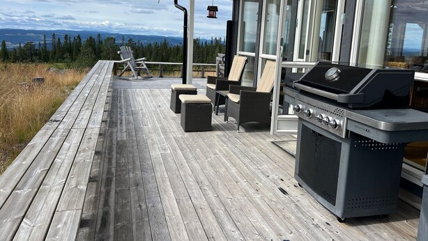 A wooden deck with outdoor furniture, a grill, and a view of the landscape. - TexasToppen, cabin in Hafjell with sauna (Øyer)