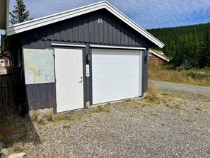 A single-story building with a dark exterior, a white garage door, and a small attached shed with a map on the wall. - TexasToppen, cabin in Hafjell with sauna (Øyer)