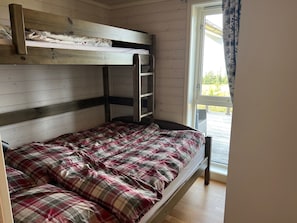Una cama individual sobre otra con tablero de cabecera de madera, colcha a cuadros y una ventana con cortinas.