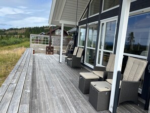 Una terraza de madera con mobiliario de mimbre y puertas de cristal.