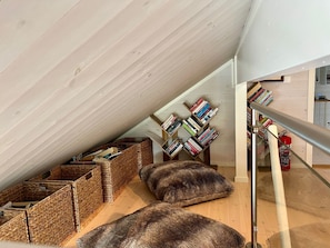 Un dormitorio tipo loft con techo inclinado, piso de madera, una escalera con barandilla metálica y estanterías empotradas llenas de libros.