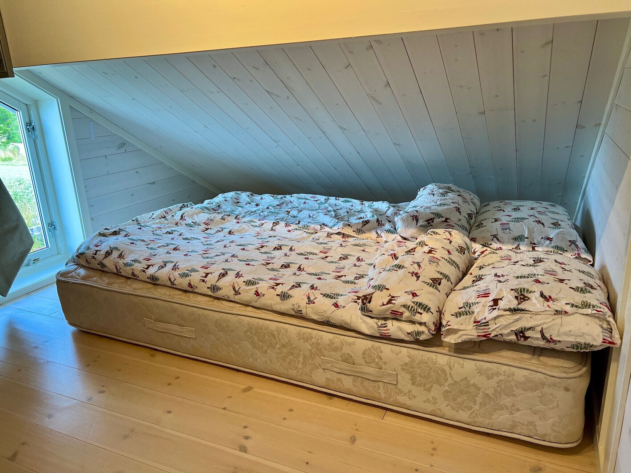 Een slaapkamer in loft-stijl met een matrasbed, een raam met uitzicht en een houten vloer.