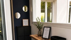 Een moderne entree met een donkere wand, een glazen deur en een houten bank met een lijstbordje en een plant.