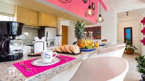 Eine moderne Küche mit einer rosafarbenen Wand, einer Kaffeemaschine, einer Obstschale und einem Frühstücksarrangement.