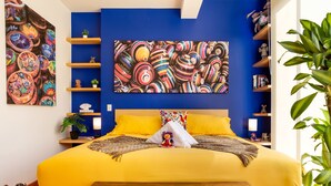 Ein Zimmer mit einem großen Bett, einer hölzernen Bank, einer Wand mit Regalen und einem großen Gemälde.