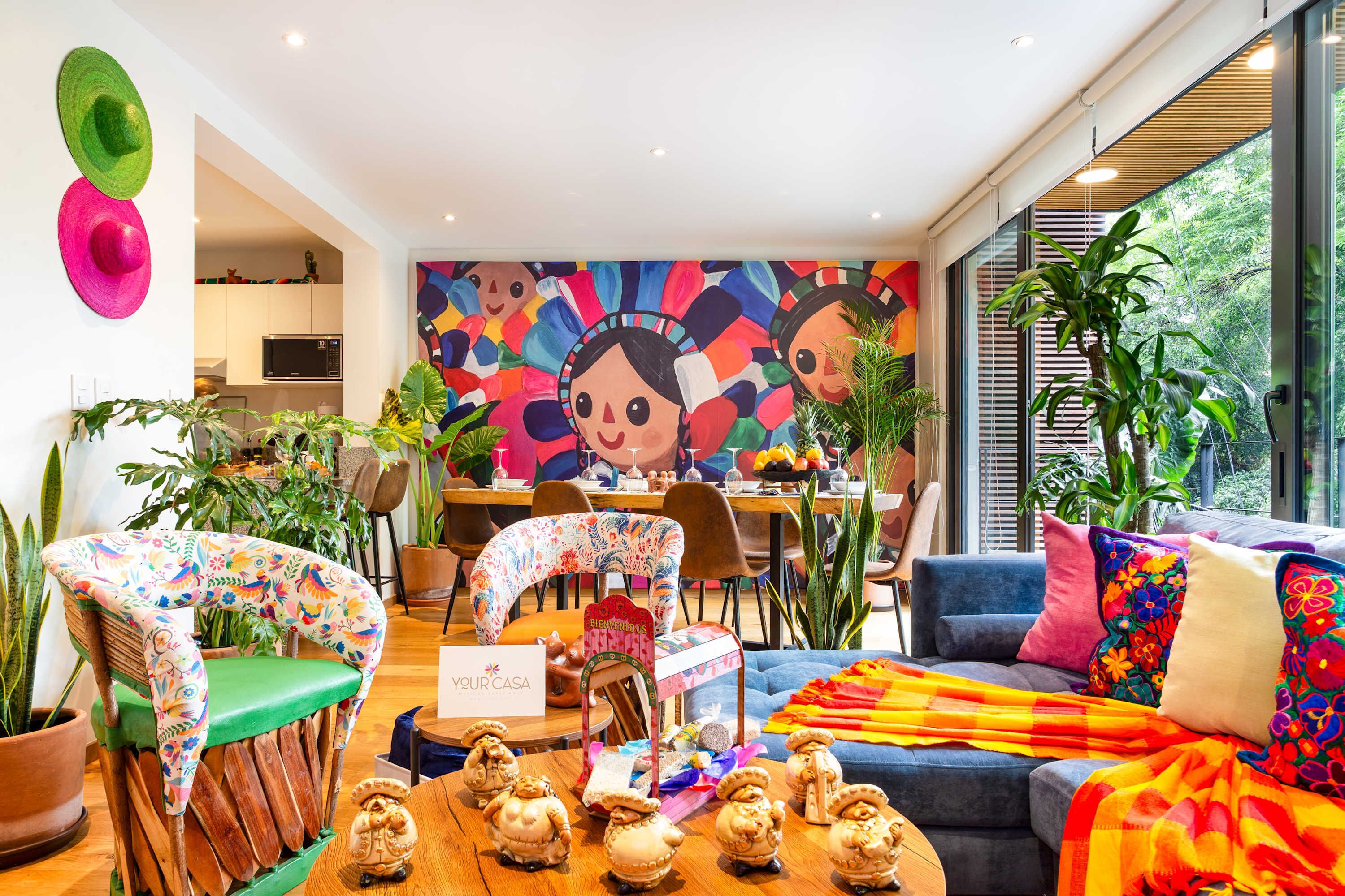 Een moderne woonkamer met een kleurrijke muurschildering, een eethoek en een keuken op de achtergrond.