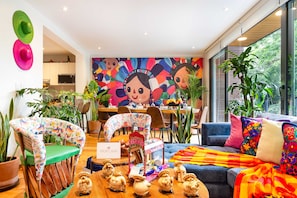 Ein modernes Wohnzimmer mit Wandgemälde, einem Essbereich und einer Küche im Hintergrund.