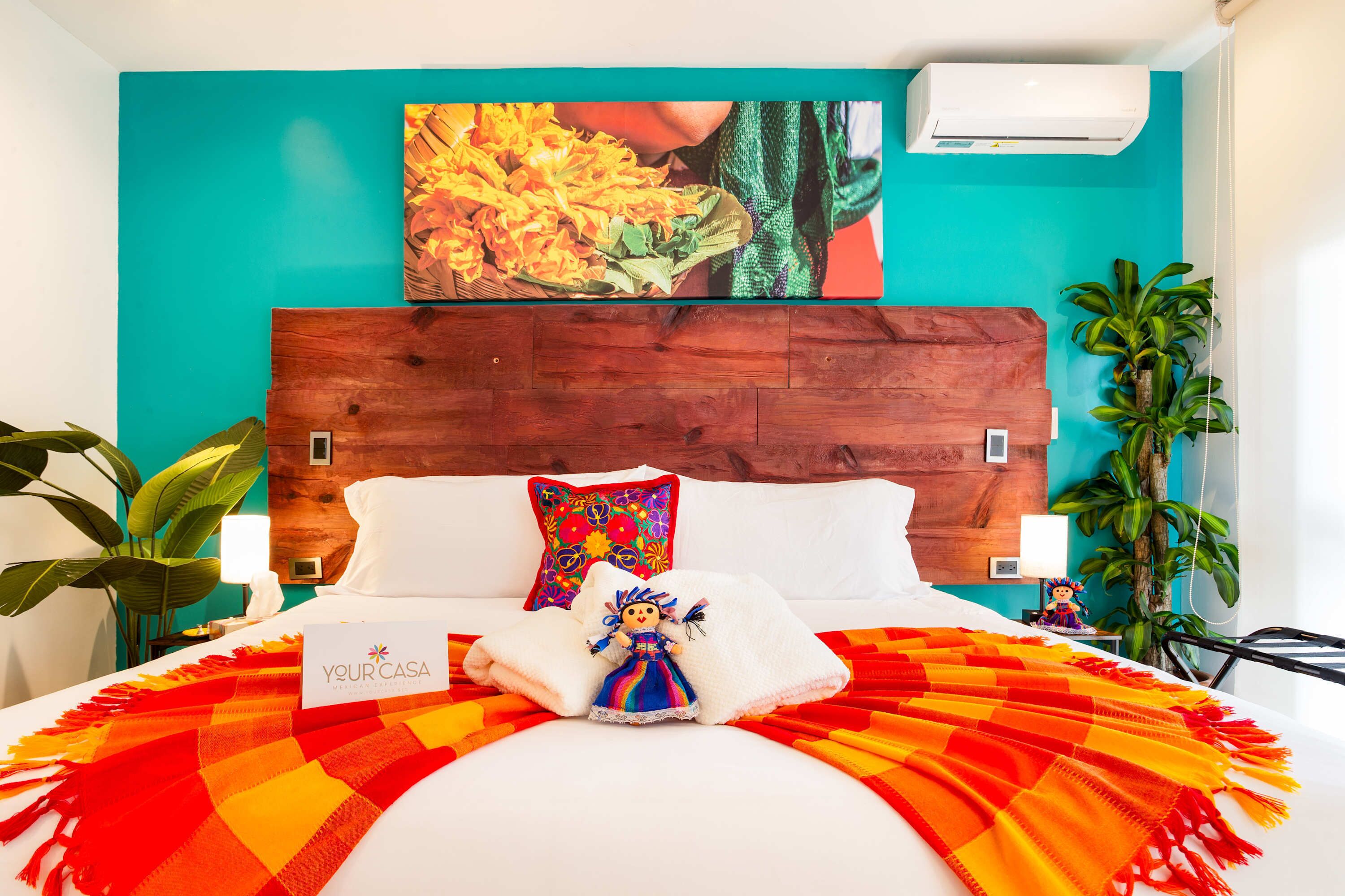A hotel room with a wooden headboard, a bed with a colorful blanket, a plush toy, and a painting on the wall.
