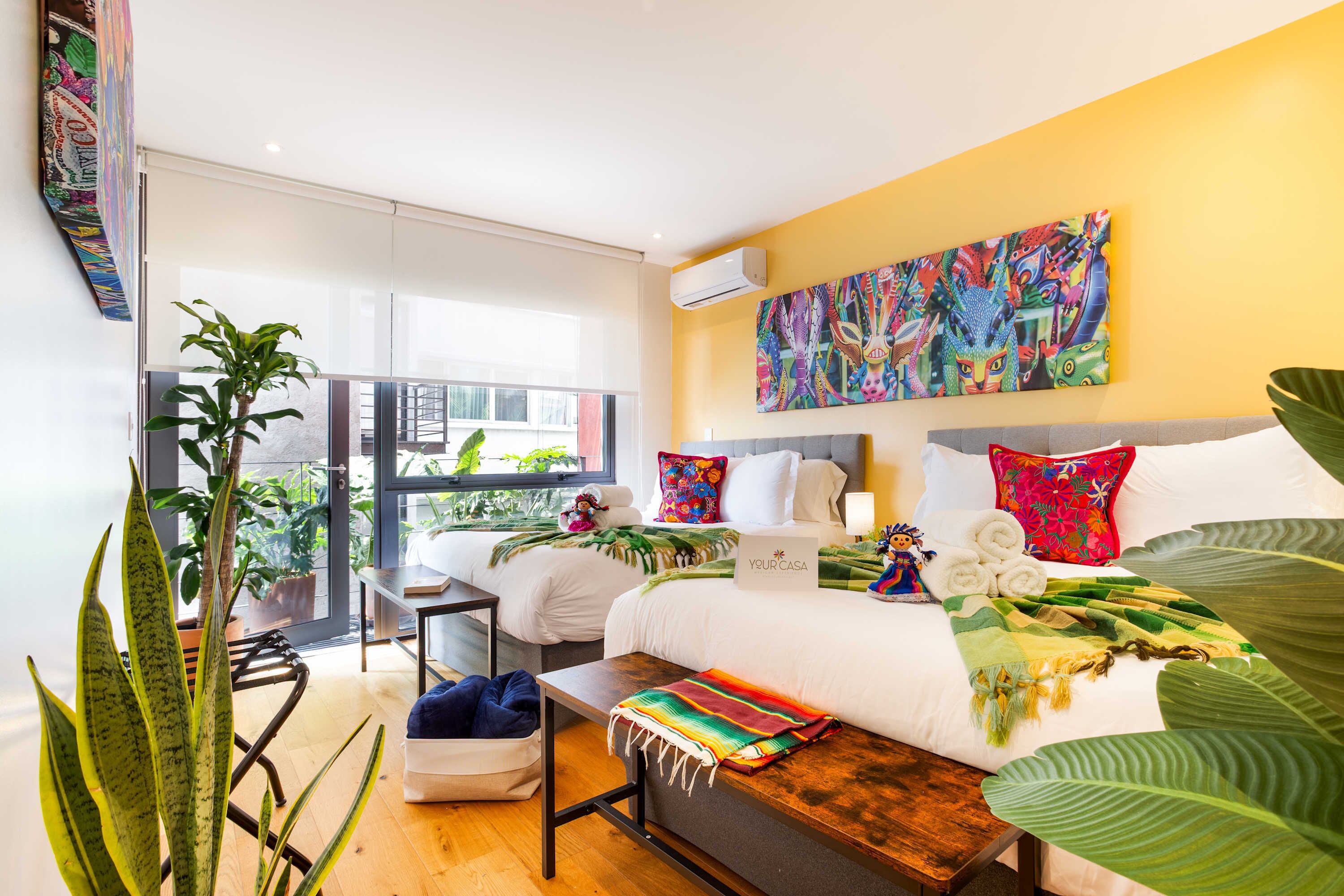 A hotel room with a bed, a desk, a chair, a window, and a large plant.