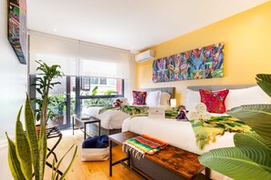 Une chambre d’hôtel avec un lit, un bureau, une chaise, une fenêtre et une grande plante.