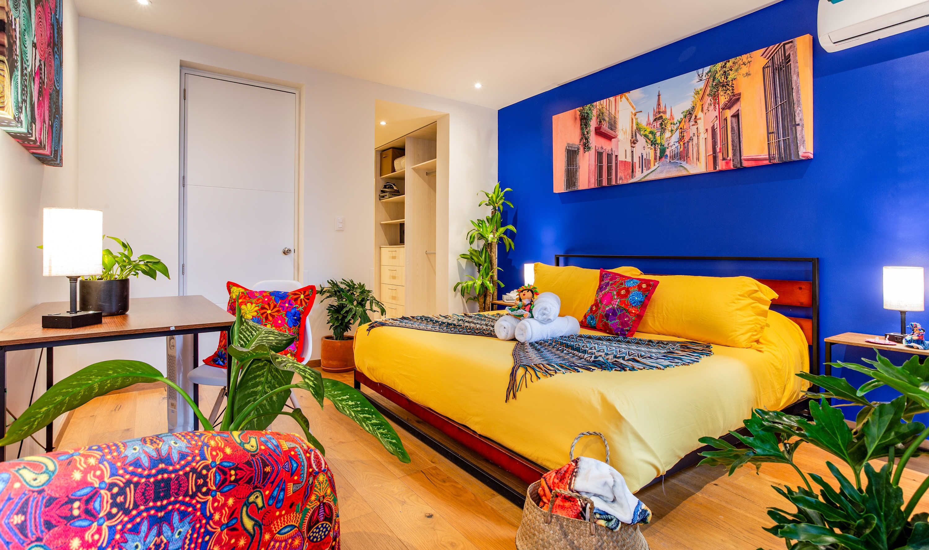 Een hotelkamer met een bed, nachtkastje, lamp, potplanten en een schilderij aan de muur.