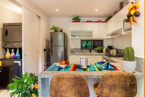 Une cuisine moderne dotée de plans de travail en granit, d’un réfrigérateur, d’une cuisinière et d’un évier. On y trouve deux chaises près de l’îlot central, une plante et un cactus sur le plan de travail.