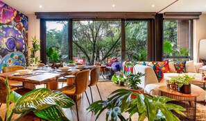 Un salon moderne avec un coin repas, de grandes fenêtres et des plantes d’intérieur.