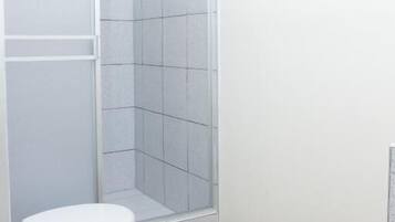 A bathroom with a white toilet, a shower with a glass door, and a white rug on the floor.