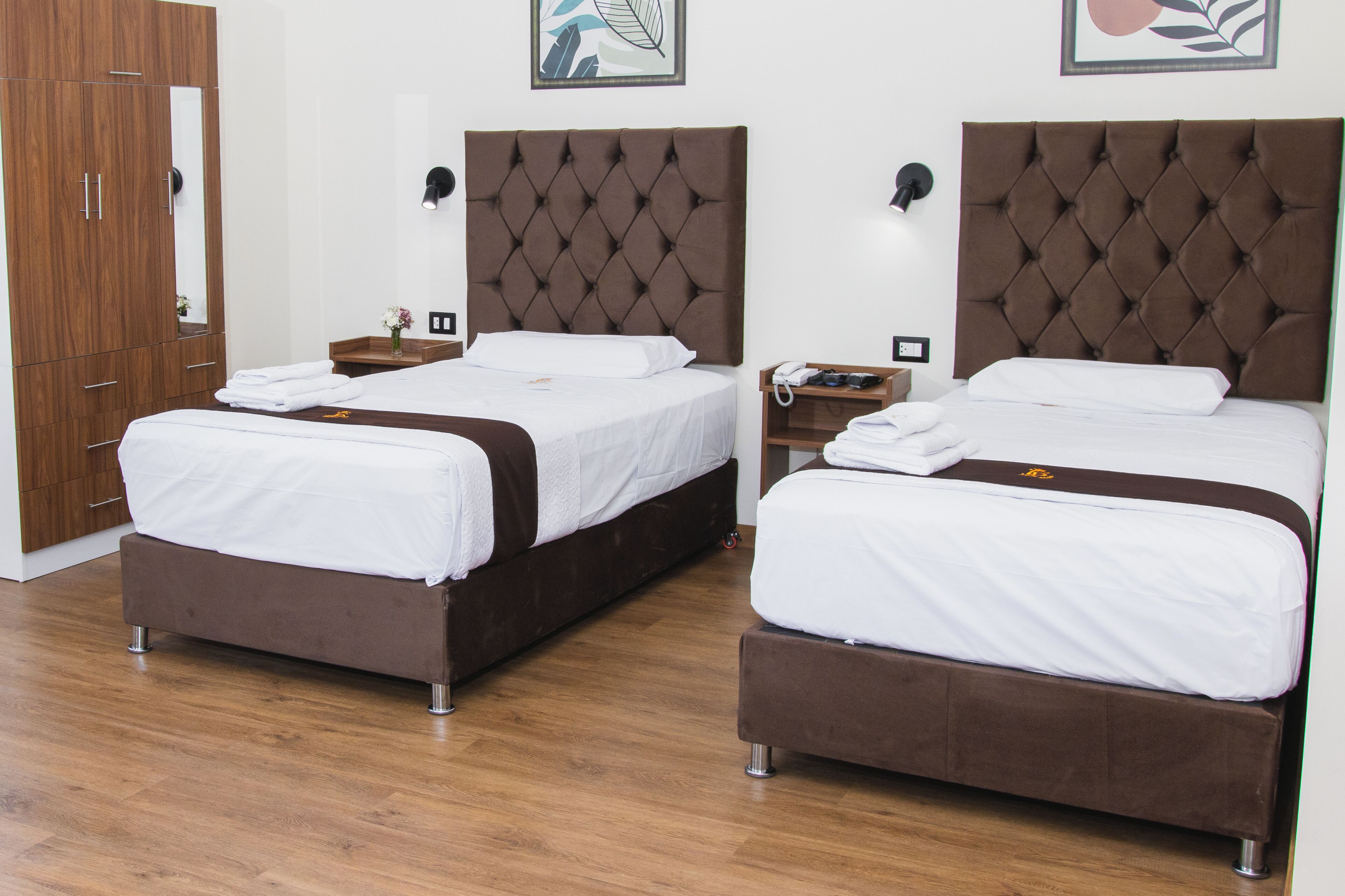Two identical twin beds with brown headboards and white bedding, wooden wardrobe, and a mirror.
