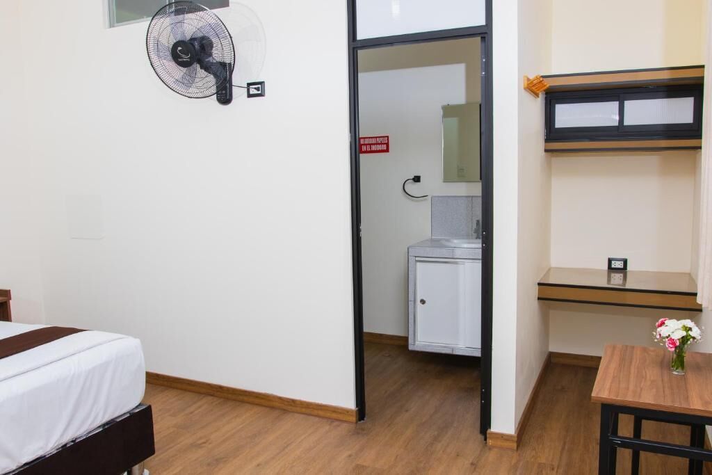 Ein Hotelzimmer mit Bett, Ventilator, einer kleinen Küchenzeile, einem Holztisch und einer Blumenvase.