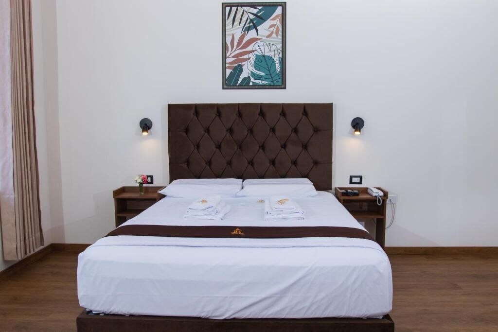 Een net opgemaakt bed met een gestoffeerd hoofdeinde, twee nachtkastjes met lampen, en een kunstwerk in een lijst erboven.