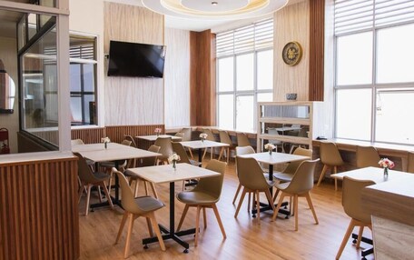 A modern dining area with tables and chairs, a flat-screen TV mounted on the wall, and large windows.
