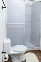 Un baño con inodoro, cabina de ducha y una alfombra blanca en el suelo.