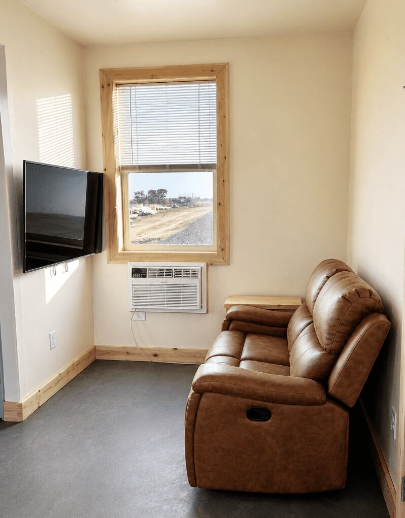 Una habitación con un sillón de cuero reclinable, un televisor de pantalla plana, una ventana con persianas y un equipo de aire acondicionado.