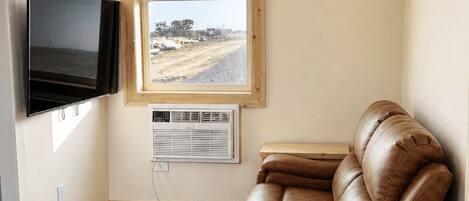 Una habitación con un sillón de cuero reclinable, un televisor de pantalla plana, una ventana con persianas y un equipo de aire acondicionado.