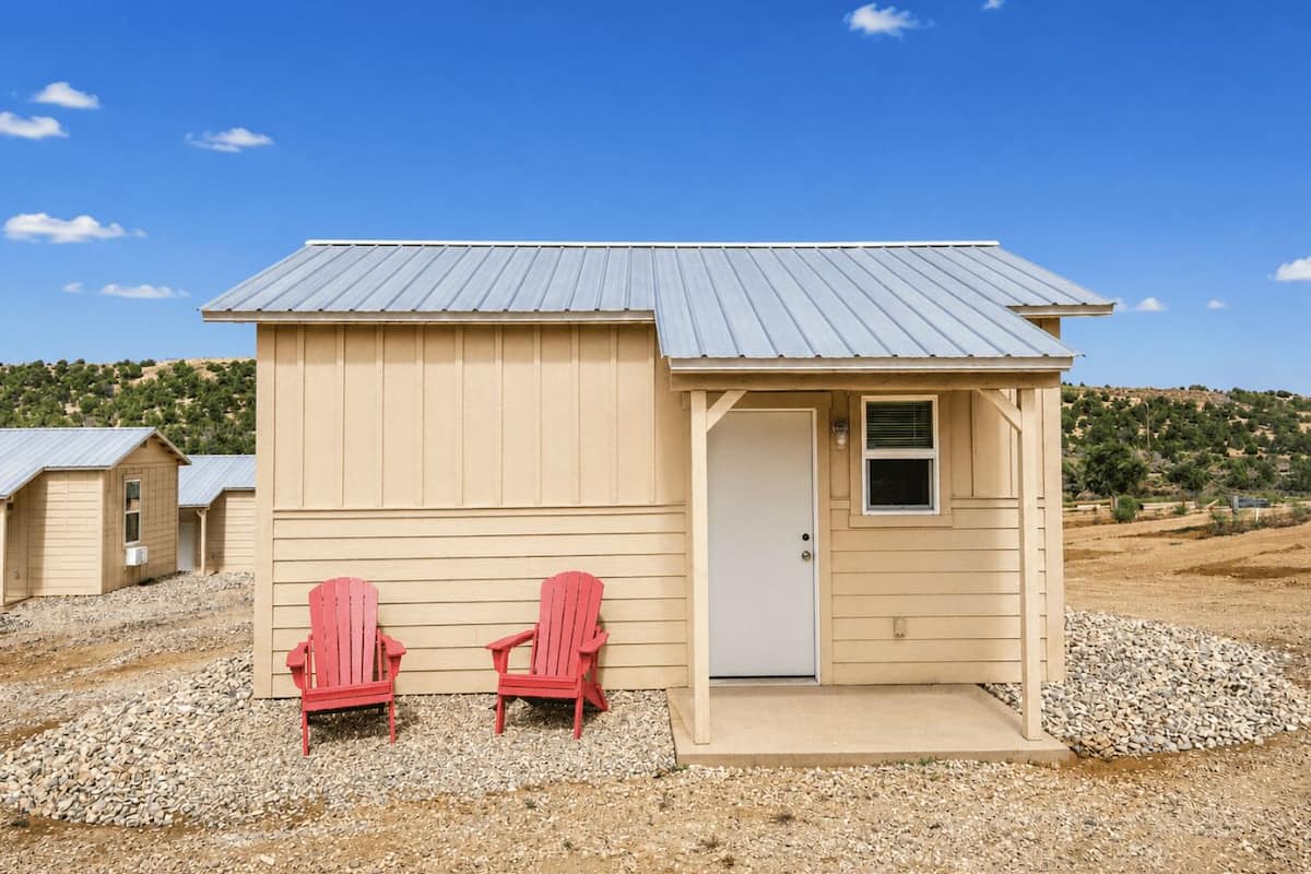 A small, single-story building with a metal roof, a door, and two red Adirondack chairs in front.