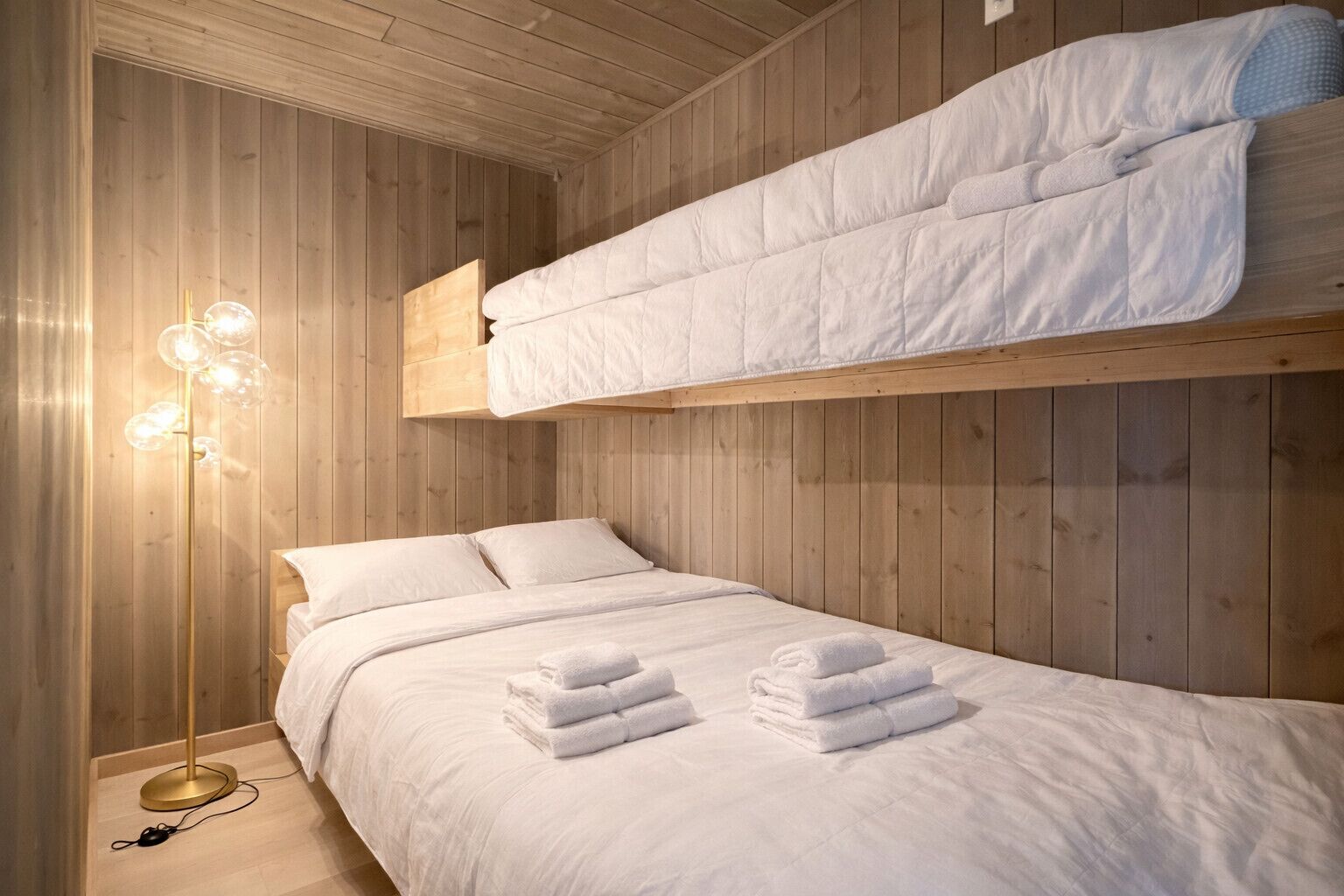 Une chambre avec des lits superposés, un plafond en bois, une lampe de chevet et des serviettes soigneusement pliées sur le lit.