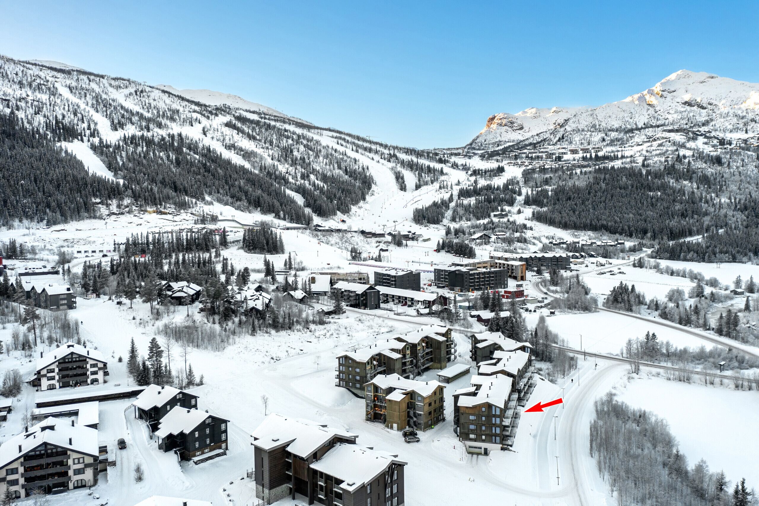 Un complejo turístico en la montaña cubierto de nieve, con varios edificios, incluyendo un refugio para esquiadores y varias construcciones de varios pisos.
