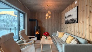 Una habitación acogedora con chimenea, paredes de madera, un sofá, sillones y un ventanal grande.