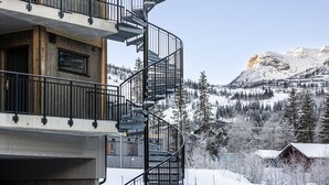 Un edificio de varios pisos con una escalera espiral, fachada de madera y vistas a montañas nevadas.