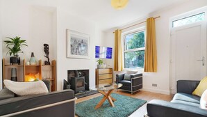 A modern living room with a sofa, a glass coffee table, a fireplace, and a large window with curtains. - Chic 3BR Rotherham Parking WIFI By stay with us (Wath upon Dearne)