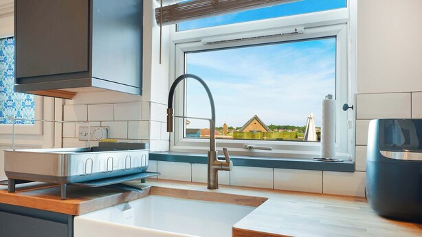 A modern kitchen with a built-in dishwasher, a stainless steel range hood, and a window with a view of houses. - Chic 3BR Rotherham Parking WIFI By stay with us (Wath upon Dearne)
