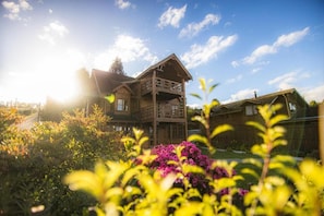A wooden cabin with a balcony, surrounded by lush greenery and flowers.