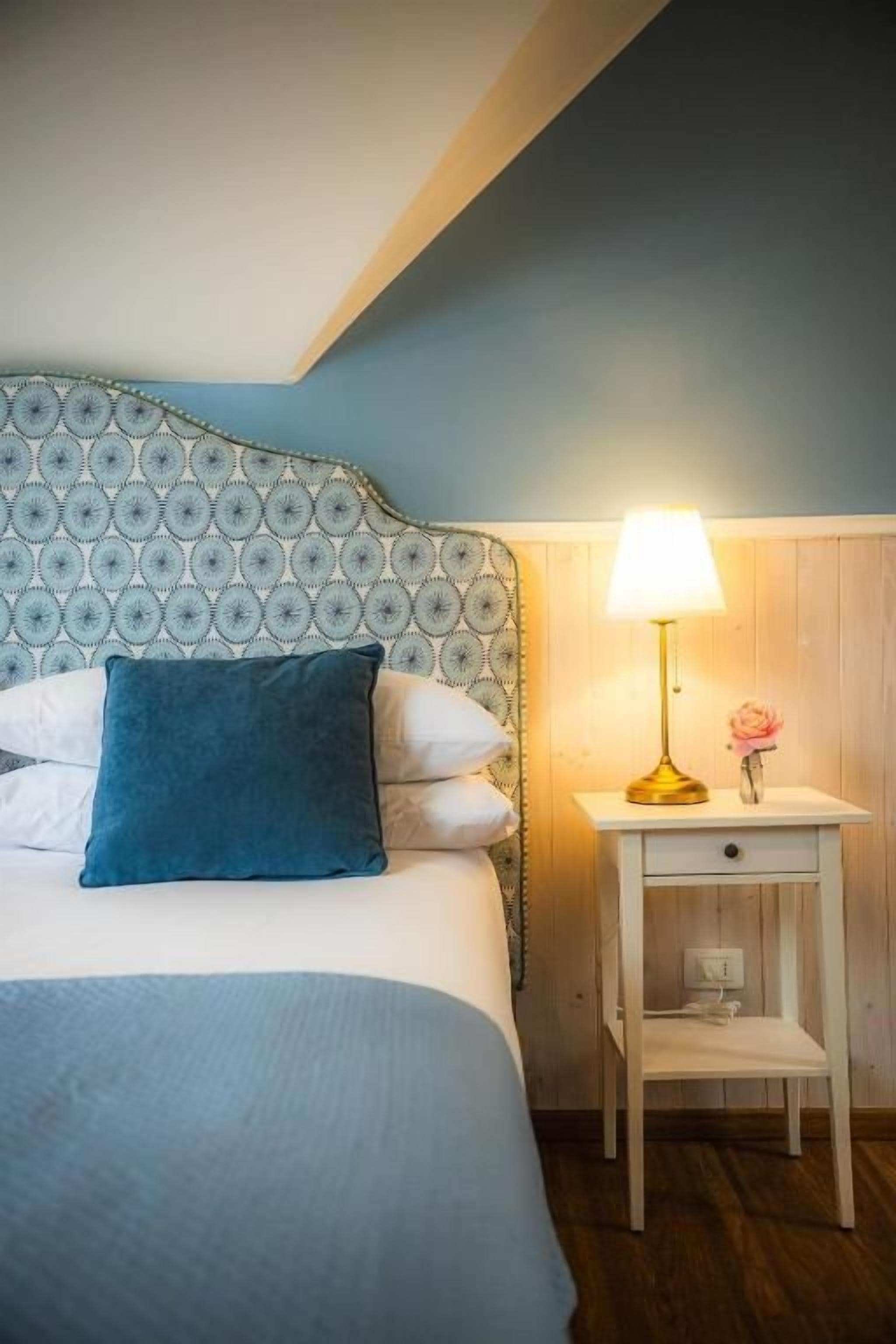 Ein Schlafzimmer mit einem gemusterten Kopfteil, einem Nachttisch mit Lampe und einer kleinen Schublade.