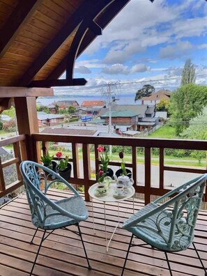 A wooden deck with two chairs and a small table, overlooking a residential area with houses and greenery.