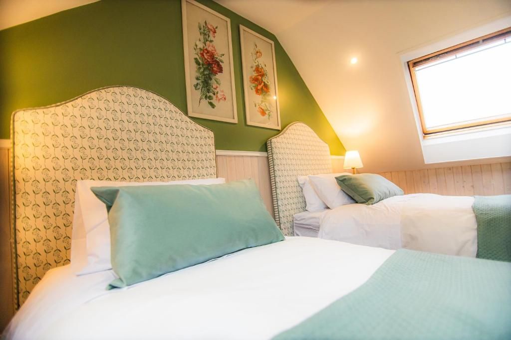 Un dormitorio con dos camas, paredes verdes, obras de arte con motivos florales y una ventana.