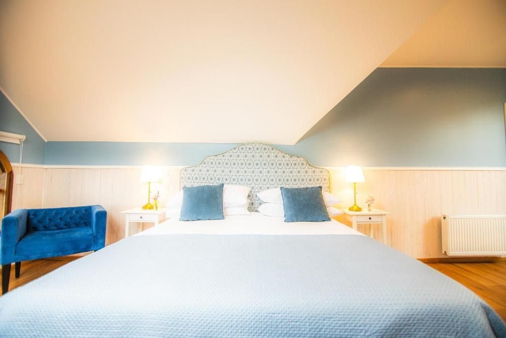 Un dormitorio con una cama grande, dos mesitas de noche, un sillón azul y un cabecero estampado.
