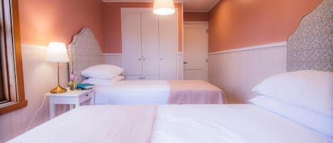 Una habitación de hotel con dos camas, una mesita de noche con lámpara y una puerta que da a otra habitación.