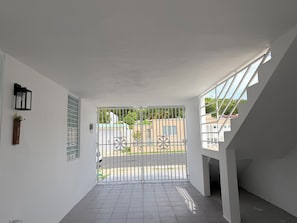 A hallway with a white door, a small plant, and a window with a view of buildings and greenery. - NEW! Family Stay near Beaches, El Yunque, BioBay & Ferry (Fajardo)