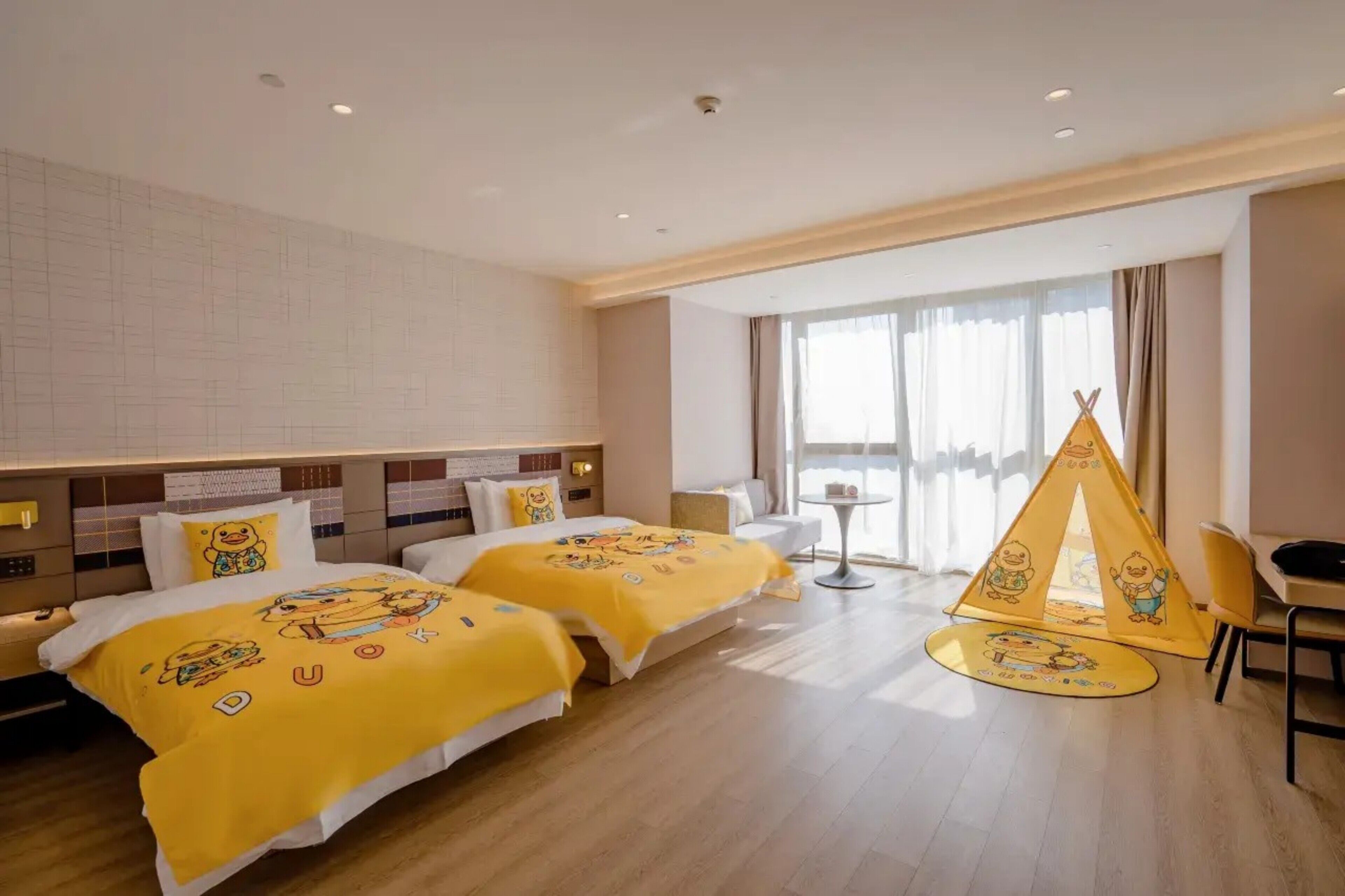 A hotel room with two beds, a small table, a chair, and a play tent.