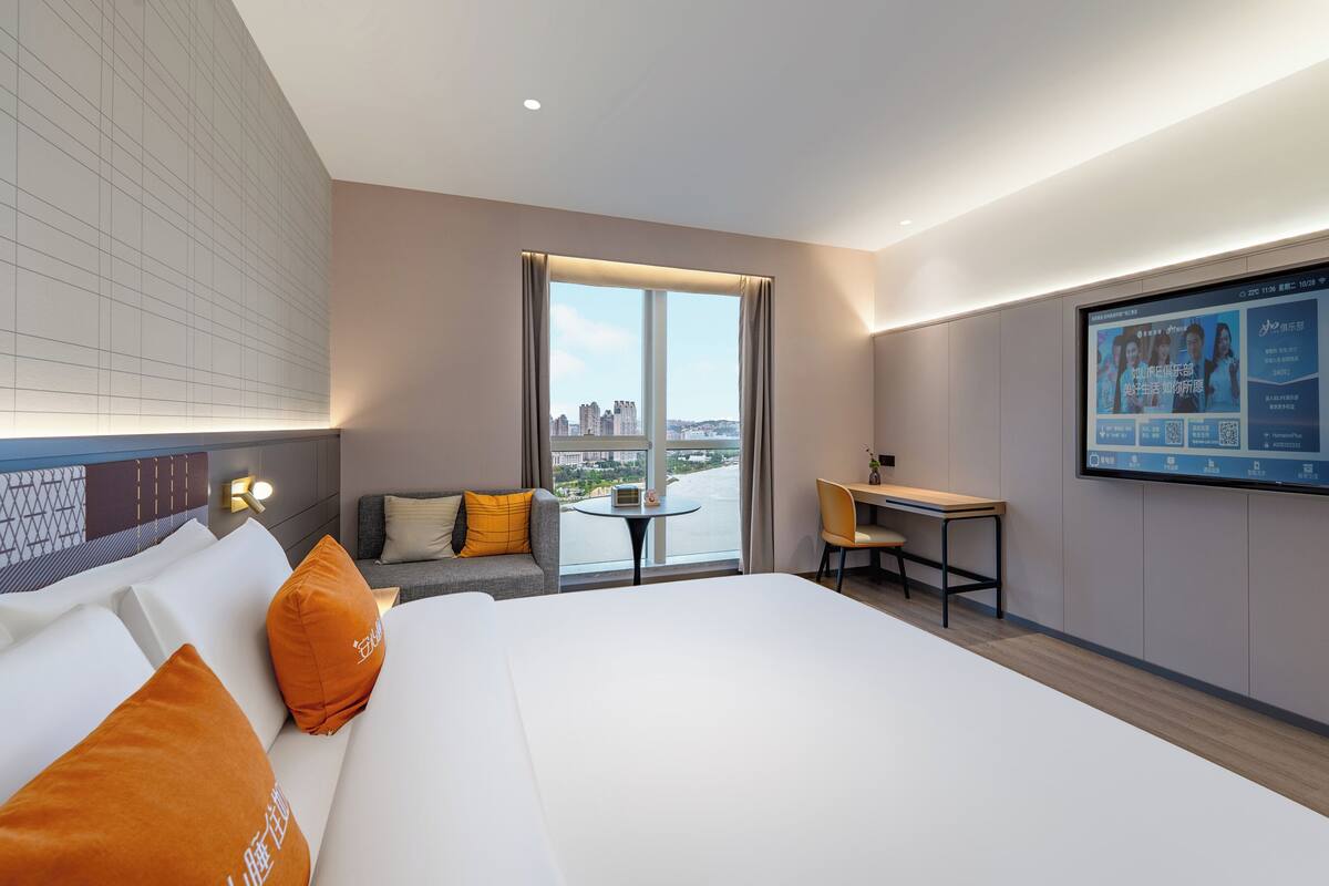A hotel room with a large bed, a desk, a sofa, and a view of the city.