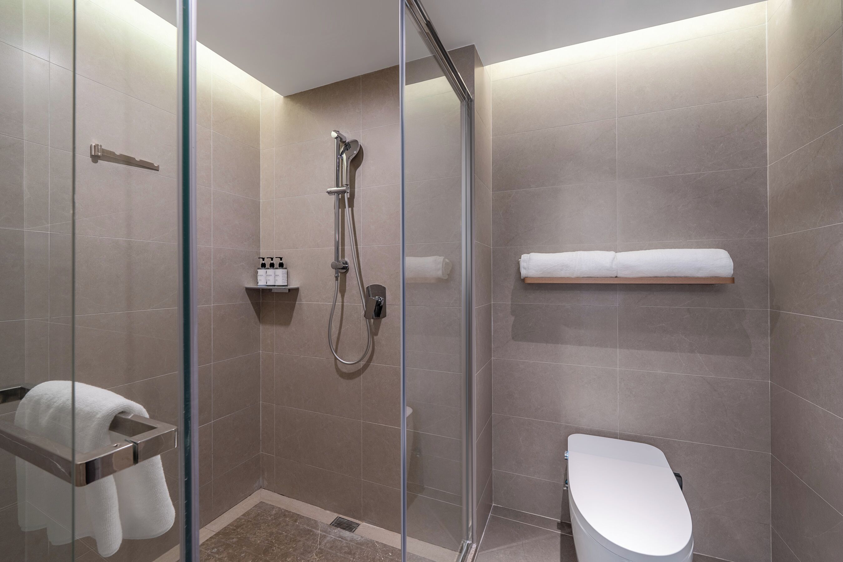 Une salle de bain moderne avec une douche à parois de verre, des toilettes blanches et un porte-serviettes.