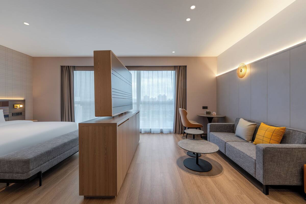 A modern hotel room with a bed, sofa, TV, and a small table.