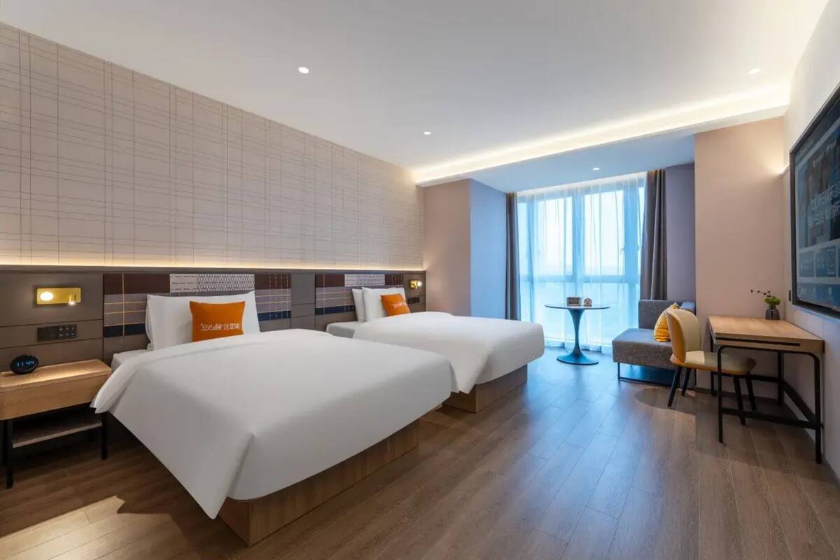 A hotel room with two beds, a desk, a chair, a small table, and a large window.