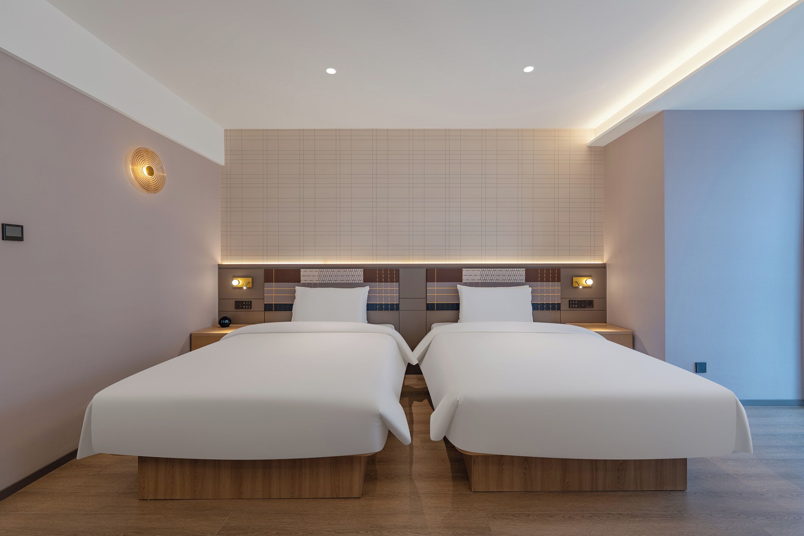 Una habitación de hotel moderna con dos camas individuales, un televisor grande montado en la pared y un estante empotrado.