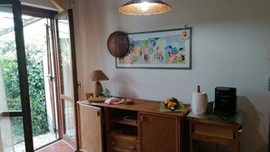 Een kamer met een schuifdeur, een geweven tafel, een wandlamp, een kleurrijk schilderij en een koffieapparaat.