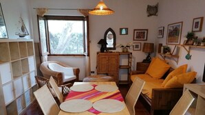 Een gezellige woonkamer met rieten meubels, een houten eettafel en een raam met uitzicht op bomen.
