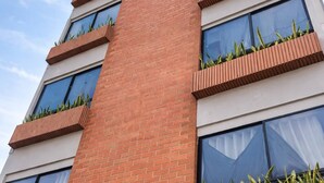 A multi-story building with a brick facade, large windows, and small balconies with plants. - Private terrace + panoramic view | Coworking (Medellín)